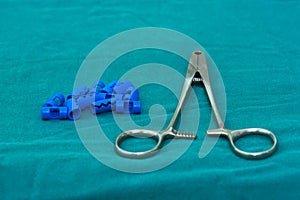 Blue plastic surgical clips and stainless applier for scalp hemostasis in brain surgery on green table in operating room