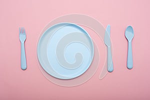 Blue plastic tableware : plate, fork, knife and spoon on pink background.