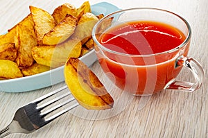 Blue plate with fried potato, piece of potato strung on fork, cup with tomato juice on wooden table
