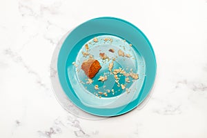 A blue plate with a piece of bread and breadcrumbs on a marble kitchen counter