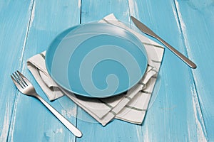 Blue Plate with utensils and dish towel on blue wooden background with perspective