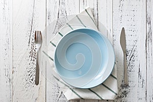 Blue Plate with utensils and dish towel on white wooden background