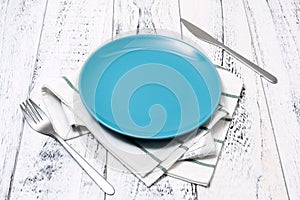 Blue Plate with utensils and dish towel on white wooden background side view