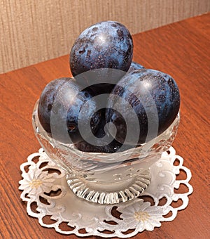 Blue plums in a glass vase.The vase stands on a napkin on the table.