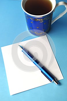 Blue porcelain china cup with blue pen and pencils, white note card and blue background