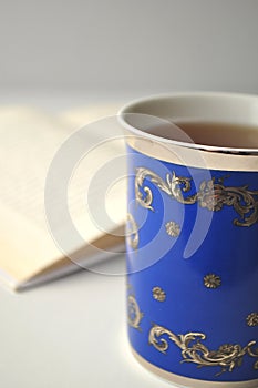 Blue porcelain china cup with tea, open book and white background