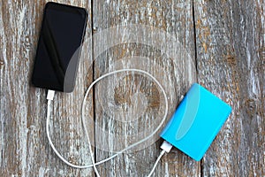 Blue power bank with white usb and black smartphone on old vintage wooden background. Modern, information technology photo