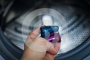 Blue and purple gel capsules for laundry putting by hand inside the washing machine