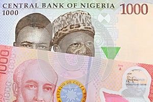 A blue, purple and green one thousand  naira note from Nigeria paired with a colorful red one thousand colones bank note from Cost