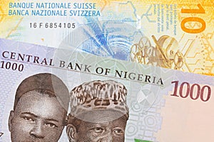 A blue, purple and green one thousand  naira note from Nigeria paired with a yellow Swiss ten franc bill.