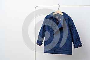 Blue quilted kids coat on hanger against white wall