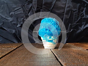 Blue raspberry Hawaiian Shave ice, Shaved ice or snow cone in a clear plastic cup with ice cream with a black background.