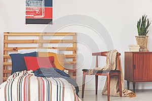 Blue, red and orange pillows on single bed with stripped duvet and wooden headboard in oldschool bedroom interior, real photo