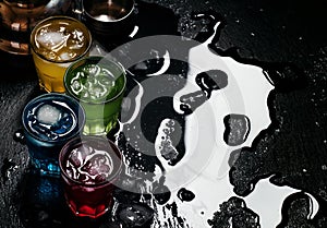 Blue, red, yellow and green cocktails with ice on a dark background, top view