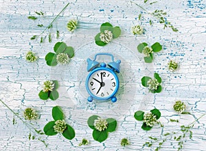 Blue retro alarm clock surrounded clover flowers