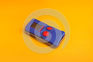 Blue retro electronic portable game console on orange background.