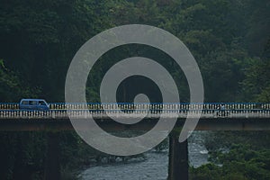 Blue retro van on a bridge over a river surrounded by trees