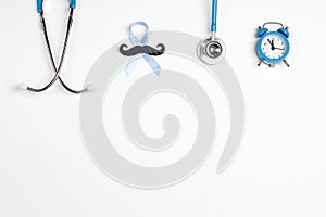 Blue ribbon with mustache, stethoscope, alarm clock and copy space on white background. Prostate cancer awareness