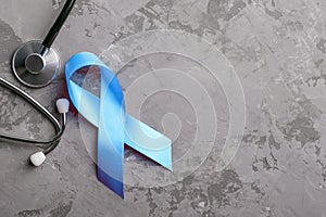 Blue ribbon and stethoscope on grey concrete background, prostate cancer awareness concept.