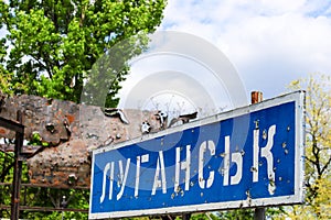 Blue road sign with the inscription in Ukrainian Lugansk, punched by bullets during the war in the Donbass, conflict East Ukraine