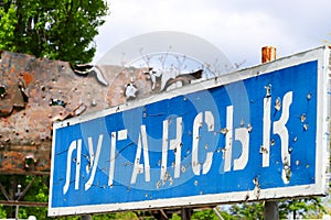 Blue road sign with the inscription in Ukrainian Lugansk, punched by bullets during the war in the Donbass, conflict East Ukraine photo