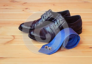 Blue rolled necktie, cufflinks and fashionable black men`s shoes on wooden background. Selective focus