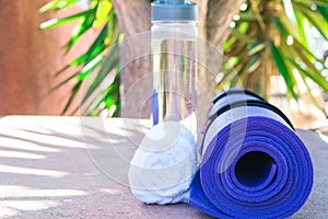 Blue Rolled Yoga Mat Bottle with Water White Towel on Greenery Palm Tree Nature Background. Sunlight. Relaxation Summer Meditation