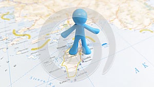 A blue rubber toy man standing on the island of Rhodes on a map of Greece