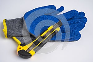 blue rubberized work gloves and a stationery knife lie on a white background