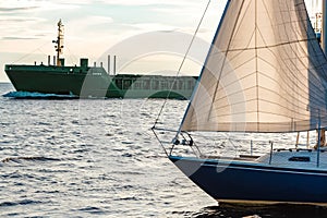 Blue sailboat against cargo ship