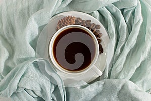 Blue scarf, coffee grains and a cup on a white table, morning start day. Autumn mood background, copy space, flat lay