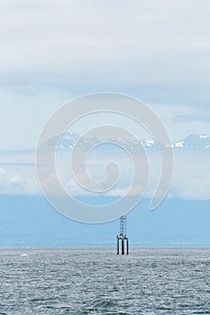 Blue scene in the Salish Sea with a navigation marker on a piling, hazy blue Olympic Mountains, sky and clouds in background, San