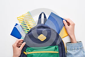 Blue schoolbag with notepad and pencil case in hands of schoolgirl isolated on white.