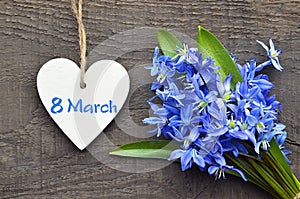 Blue Scilla flowers and decorative wooden heart on old wooden background for 8 March International Women`s Day.