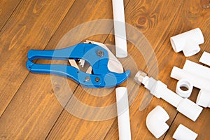Blue scissors for cutting plastic pipes, next to the corners and adapters for them, on a wooden background