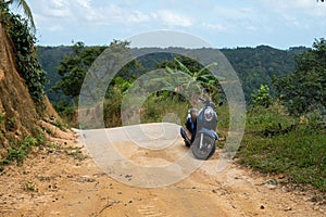 Blue scooter on the dirt road on a hill in tropical jungle with a scenic view on a mountains in a sunny day. Adventure