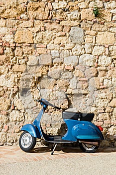 Blue scooter by the stone wall in an old town in Tuscany