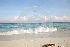 Blue sea with foam wave, white sand with footprints on the beach and blue sky with clouds on the horizon