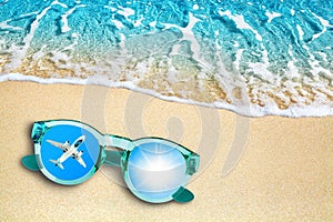 Blue sea wave, sand beach, turquoise ocean water, sunglasses, mirror reflection of airplane flight and shiny sun in sky top view