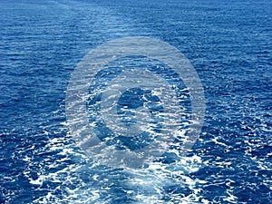 Blue sea waves with white foam. Water behind a ship. Boat wake in the sea, on a brilliant sunny day