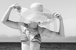 Modern woman on seashore hiding behind beach straw hat