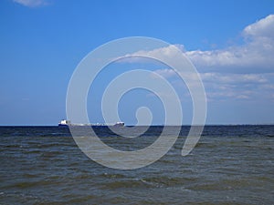 Blue shades horizon. Cargo ship against cloudy blue sky and rippled sea