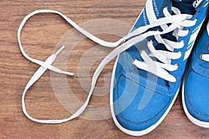 Blue shoes with unbound lace in the shape of a heart on a wooden floor