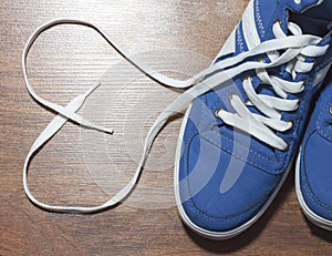 Blue shoes with unbound lace in the shape of a heart on a wooden floor