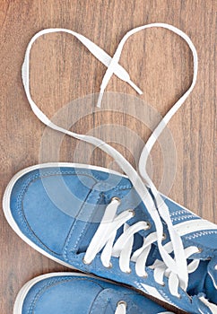 Blue shoes with unbound lace in the shape of a heart on a wooden floor