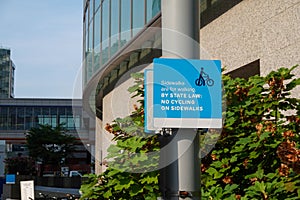 Blue sign on a light post that says that sidewalks are for walking and prohibits bike riding on the sidewalk photo