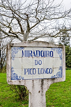 Blue sign Miradoiro do Pico Longo, Viewpoint Pico Longo in English, on typical Portuguese tiles. Grass and trees without photo