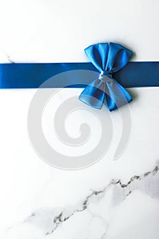 Blue silk ribbon and bow on luxury marble background, holiday flatlay backdrop