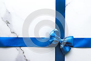 Blue silk ribbon and bow on luxury marble background, holiday flatlay backdrop