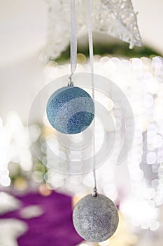 Blue and silver baubles hanging on unfocused background with shiny sparkling garland lights and bokeh. Christmas tree toys